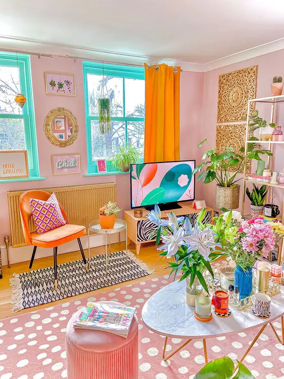 a dopamine decor living room with pink walls, turquoise windows, an orange chair, a pink printed rug, pink pouf and some blooms and greenery