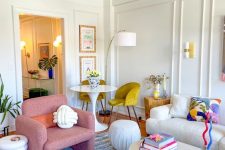 a dopamine decor living room with white furniture and a pink accent chair, a dining table and mustard chairs, bright decor and a rug