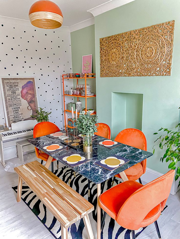 a dopamine dining space with a mint and spotted accent wall, a marble table, orange chairs and a shelving unit, greenery