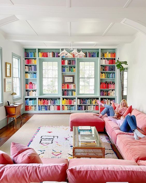a dopamine living room with an aqua wall done with bookshelves and colorful pillows, a large pink sofa, layered rugs and greenery