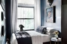 a dramatic and small bedroom with dark walls and a ceiling, dark and chic furniture, a cluster chandelier and a gallery wall