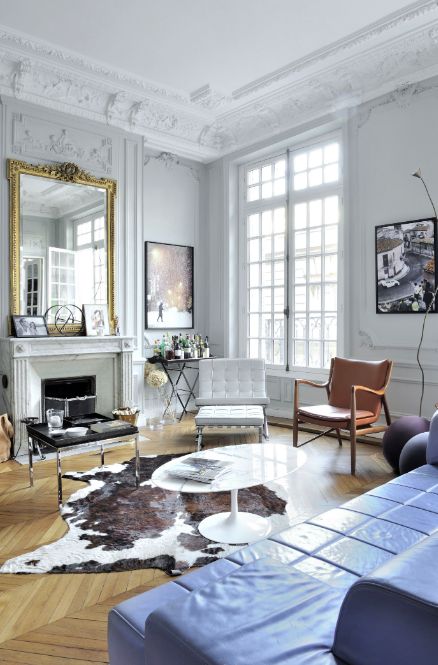 a gorgeous Parisian living room with molding and chevron floors, a fireplace, an oversized mirror, a  blue sofa and orange chair