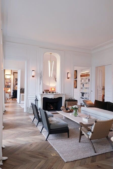 a gorgeous Parisian space with molding and chevron parquet, a fireplace, a white sofa and black chairs, a coffee table and a cool lamp