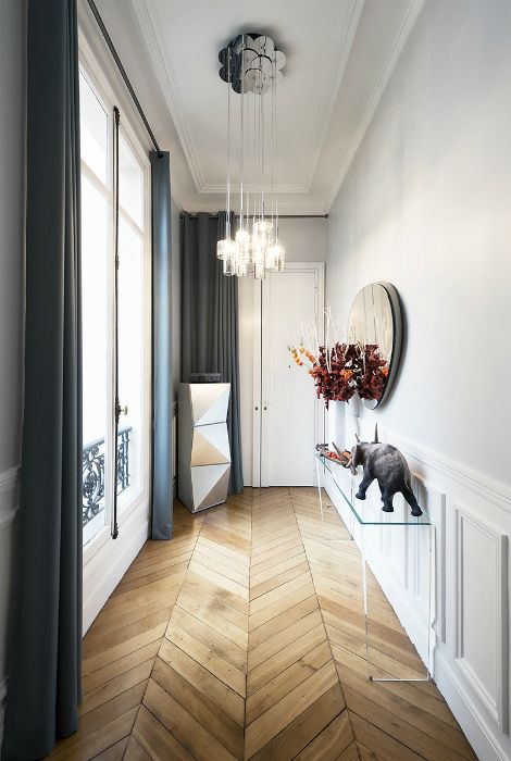 a gorgeous corridor with chevron parquet floors, a clear console table, pendant lamps and some decor