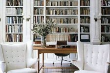 a gorgeous white home office with arched bookcases, a stained desk, a brown chair, creamy wingback chairs and a rug
