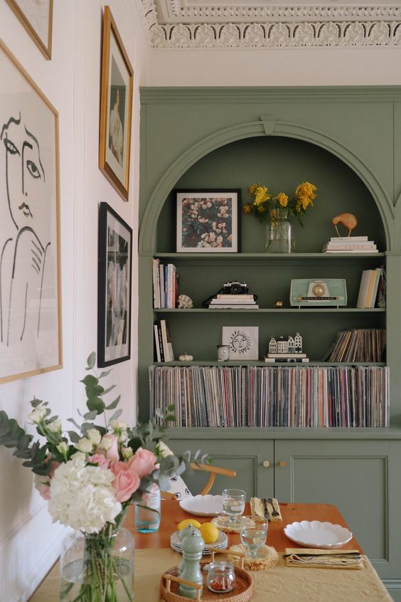 A green built in arched bookcase, a dining table, chairs and a gallery wall, some blooms and decor are amazing