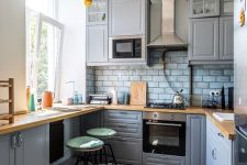 a grey kitchen with a grey tile backsplash and butcherblock countertops plus tall stools is a lovely space for cooking and eating