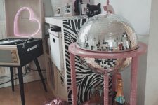 a little home bar styled as a disco ball in a pink stand, with glasses and a bottles and everything else hidden inside