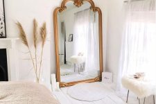 a lovely Scandinavian bedroom with an oversized mirror in a gilded frame, a bed, a fireplace and some Moroccan-style rugs