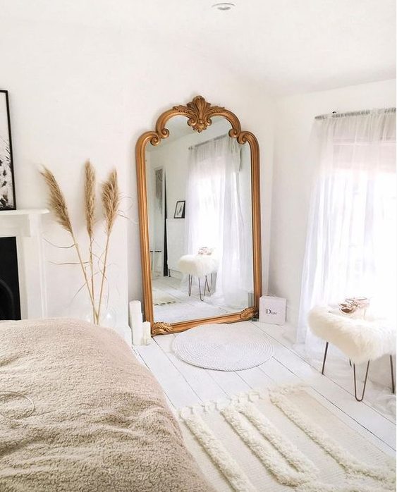 A lovely Scandinavian bedroom with an oversized mirror in a gilded frame, a bed, a fireplace and some Moroccan style rugs