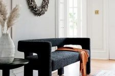 a lovely and pretty black boucle loveseat, a dried leaf wreath, a black side table for a chic and lovely space