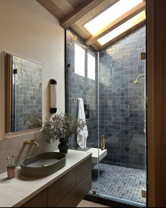 a lovely attic bathroom with a skylight, a shower space clad with grey Zellige tiles, a vanity with a grey sink