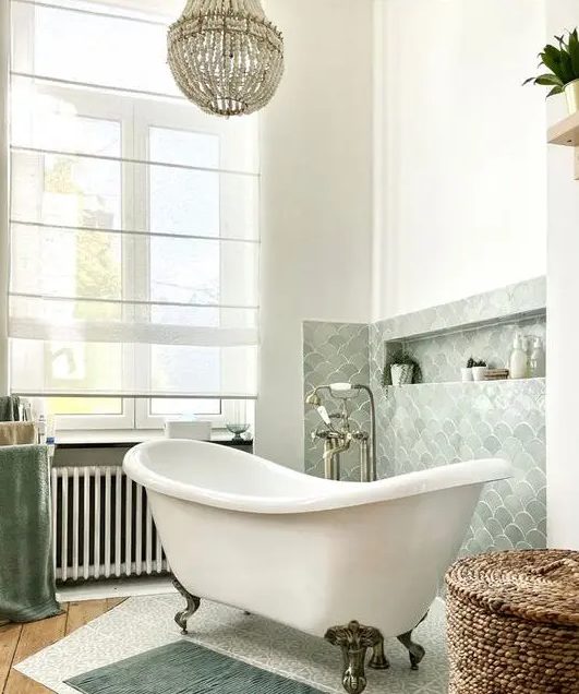 a lovely bathroom with a pale green fish scale backsplash, a free-standing tub, a basket and some rugs