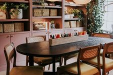 a lovely dining space and home office with a row of built-in pink arched bookcases with built-in lights, greenery and baskets, a black table and chairs