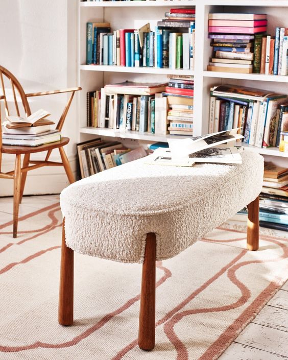 a lovely reading space with a bookcase, a stained woo vintage chair and a white boucle bench is a cool nook