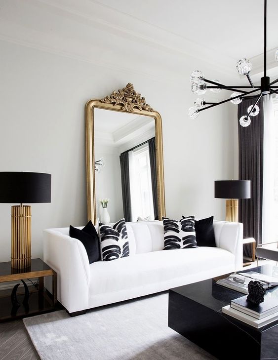 a luxurious black and white living room with a white sofa and printed pillows, a black table, a mirror in a gold frame and chic lamps