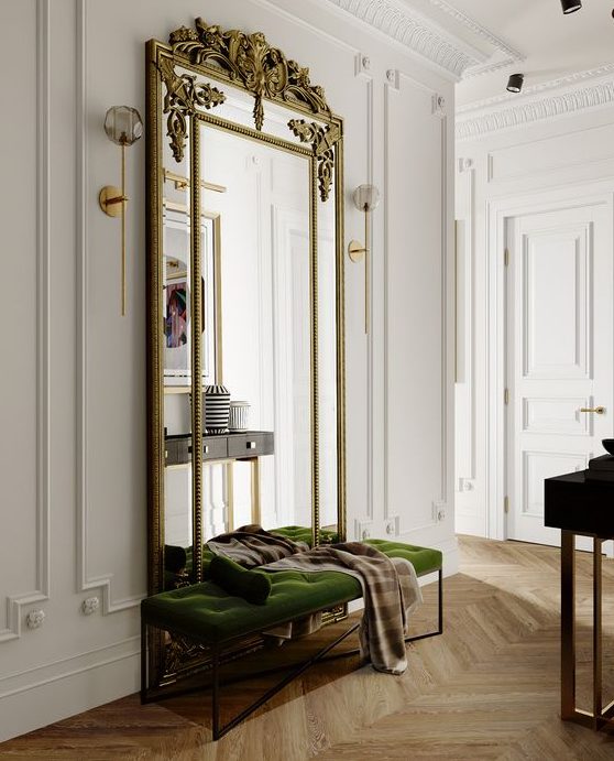 a luxurious entryway with a green velvet bench, an oversized mirror in a refined gilded frame and a dark console table