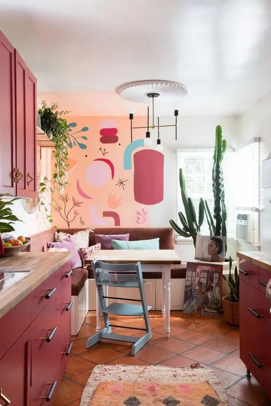 a matte burgundy kitchen with butcherblock countertops, bright wall art, a banquette seating and a table plus some potted plants
