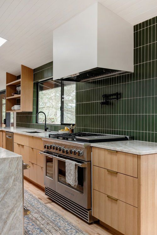 A mid century modern kitchen with stained cabinets, a green stacked tile backsplash and black fixtures