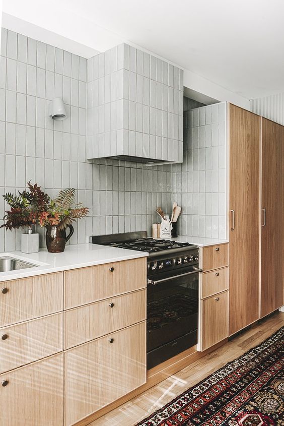 A mid century modern kitchen with stained cabinets, grey stacked tiles and white countertops