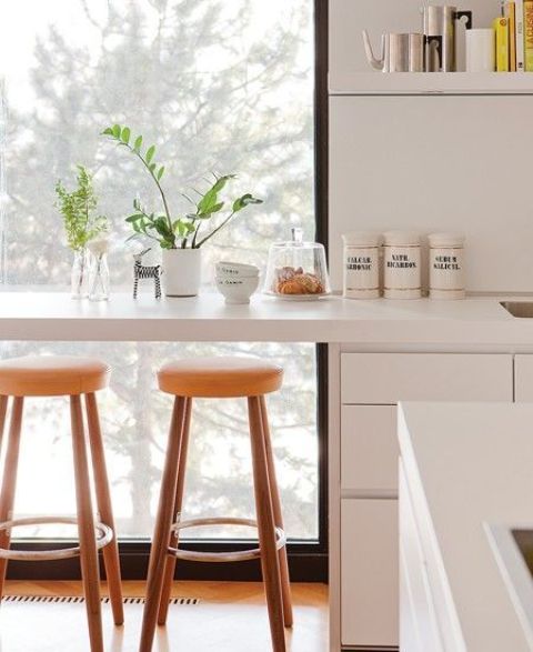 a minimal white space with a windowsill tabletop for eating, open shelves and tall stained stools plus a lovely view