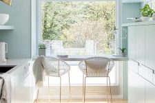 a mint blue kitchen with sleek cabients, white stone countertops, a large window and a breakfast bar with tall white stools
