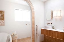 a modern Mediterranean bathroom with a tub, a window, a fluted vanity, a skylight and terracotta tile on the floor