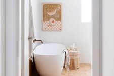 a modern Mediterranean bathroom with a window, a terracotta tile floor, an oval tub, a stool and an artwork