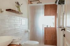 a modern bathroom clad with white skinny tiles and terracotta ones, a tile clad vanity, a shower space and a shelf