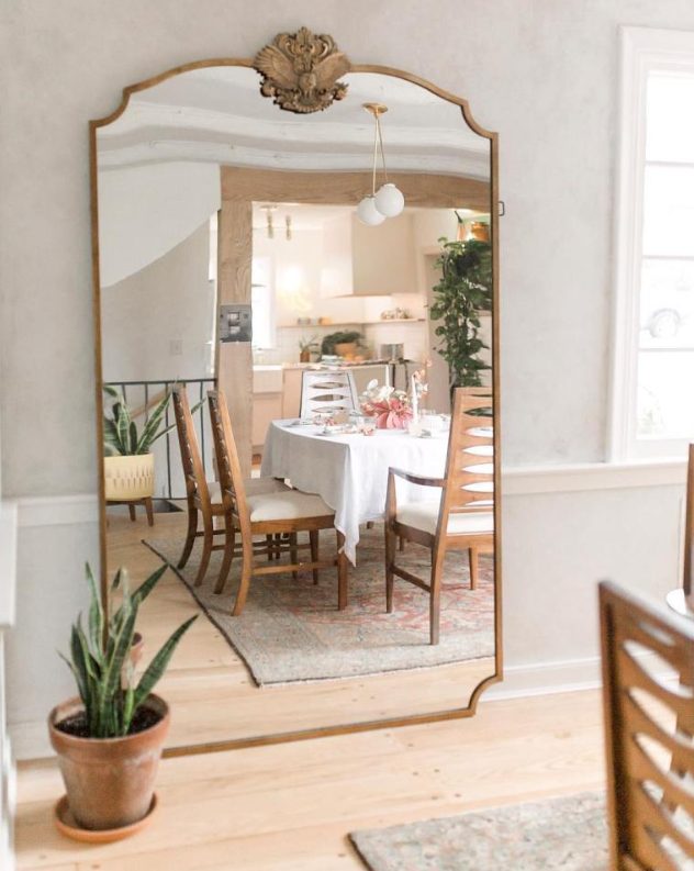 a modern farmhouse dining space with an oversized mirror in a vintage frame that reflects light and makes the space larger