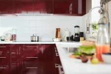 a modern glossy burgundy kitchen with a white square tile backsplash and white stone countertops is an awesome space