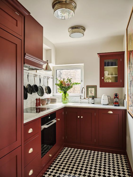 a modern kitchen in burgundy, with white stone countertops and a backsplash, a checked floor and some greenery