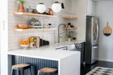 a modern kitchen with blue cabinets, white countertops, a white stacked tile backsplash, stained shelves and pendant lamps