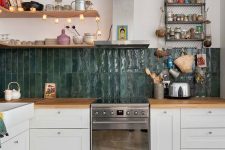 a modern kitchen with white cabinets, butcherblock countertops, a dark green stacked tile backsplash and metal shelves