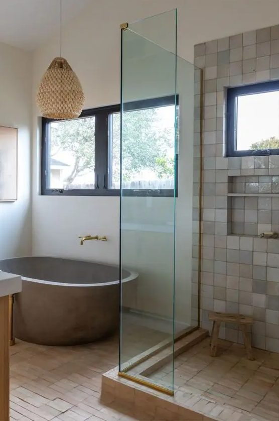 a modern rustic bathroom clad with terracotta tiles and neutral Zellige ones, an oval stone tub, a woven pendant lamp