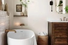 a modern rustic bathroom with white plaster walls and a terracotta tile floor, a stained vanity, an oval tub and greenery