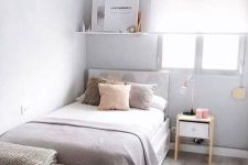 a narrow bedroom done in dove grey, with a bed and neutral bedding, a shelf ith decor, some nightstands