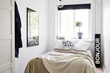 a narrow bedroom in neutrals and black, with a black sign, a pendant lamp and a black pouf is a cool idea