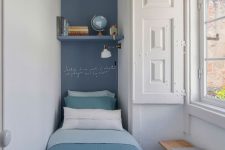 a narrow bedroom with a navy accent, a single bed with blue bedding, a shelf and some shutters is cool