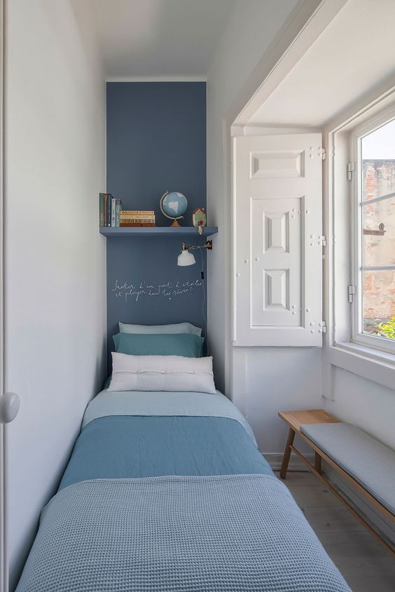 a narrow bedroom with a navy accent, a single bed with blue bedding, a shelf and some shutters is cool