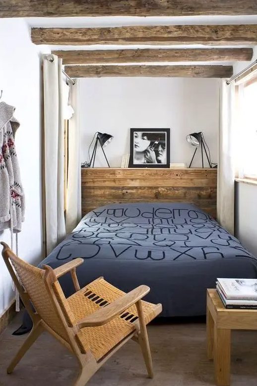 a narrow bedroom with a reclaimed wood headboard as a nightstand, wooden beams, a chair, a table with books