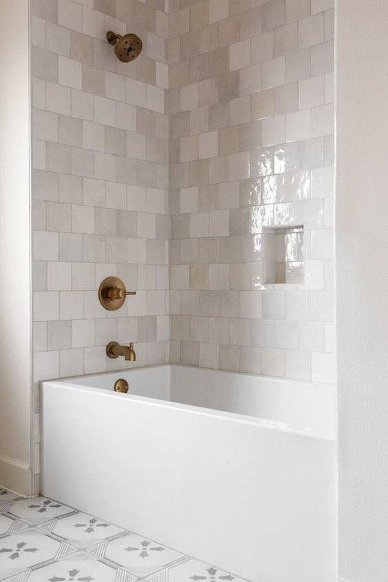 a neutral bathroom clad with square Zellige tiles, a rectangular tub, a niche and brushed brass fixtures