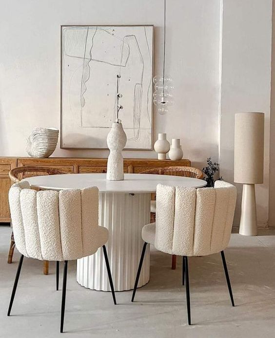 A neutral dining room with a light stained credenza, a round table, creamy boucle chairs and a pendant lamp over the table