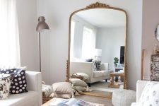 a neutral farmhouse living room with neutral furniture, printed pillows and an oversized mirror in a gilded frame is amazing