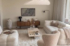 a neutral living room with a white sofa, a matching loveseat, a white boucle chair, a coffee table, a stained credenza