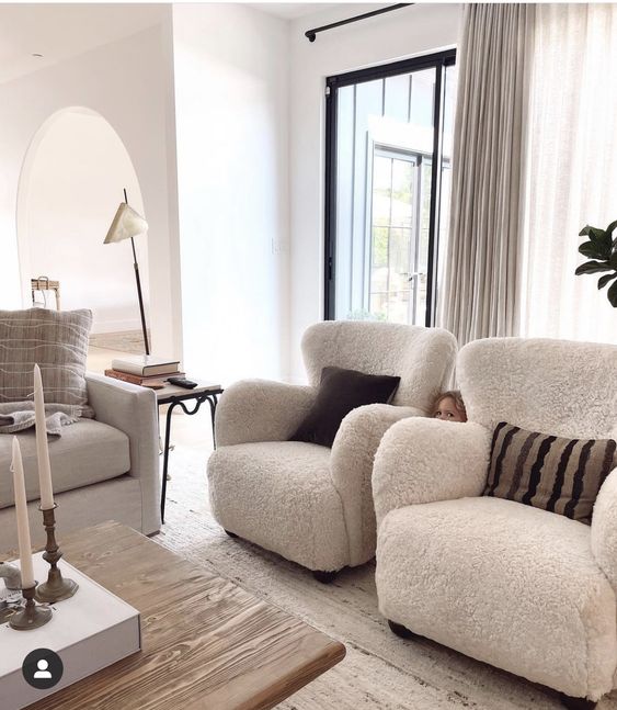 a neutral living room with a white sofa, white boucle chairs, printed pillows, a stained coffee table and some candles