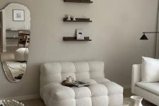 a neutral living room with white boucle seating furniture, a stone coffee table, small shelves and a mirror