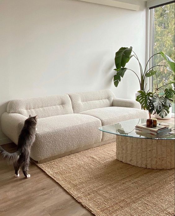 a neutral low boucle sofa, a textured rug, a table with a base made of cork and some greenery in planters for a trendy space