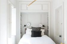 a neutral narrow bedroom with built-in shelves at the headboard, a bed with black and white bedding, a chandelier and some bright decor
