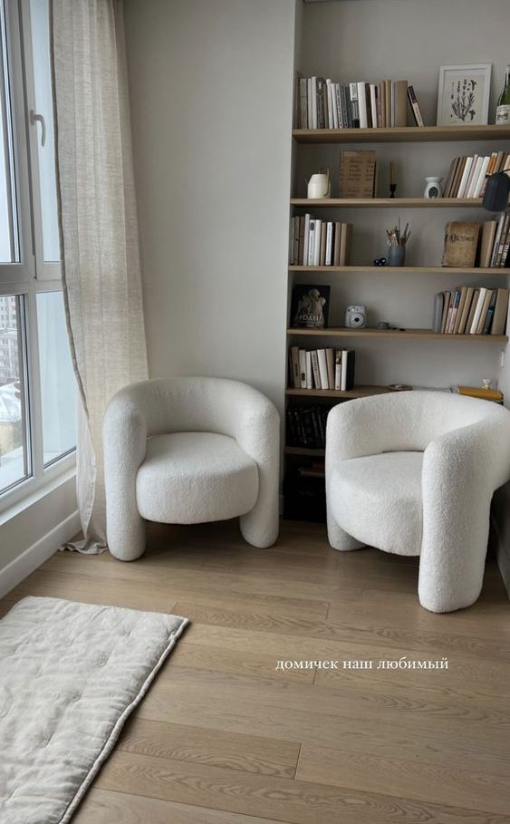 A neutral reading nook by the window, with built in shelves, white boucle furniture and a dog blanket on the floor